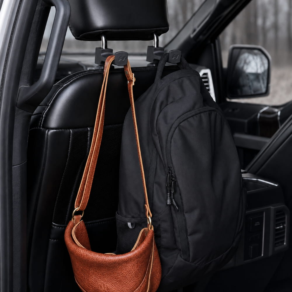 Car interior with a brown handbag and black backpack hanging from a hook on the back of the front seat.