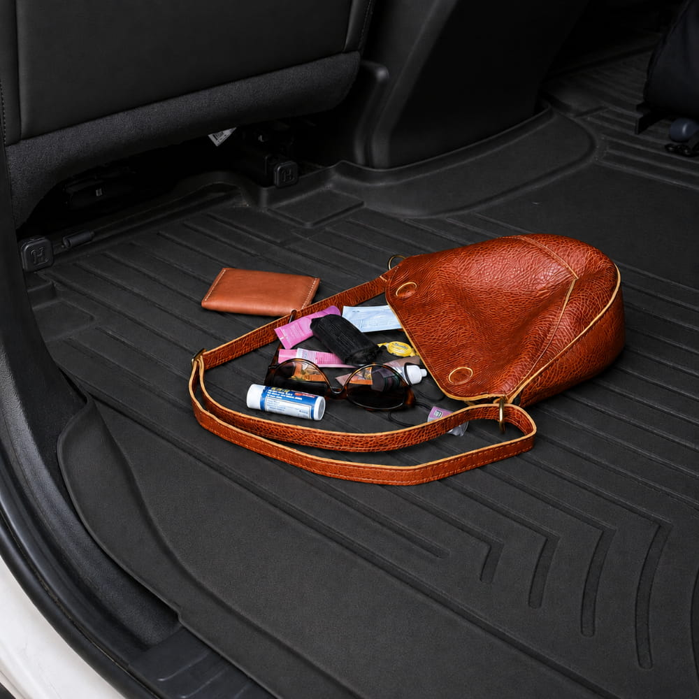 Brown leather handbag with items on a black car interior floor mat
